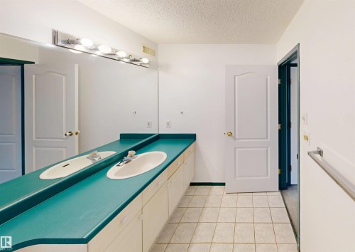 Dual vanity with integrated sinks, full-width mirror, overhead bar lighting, and tiled flooring - 10941 81 Avenue Nw, Edmonton, AB 