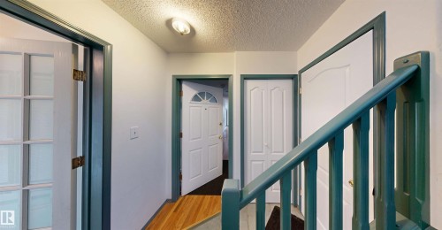 Wood-finish flooring with a white paneled door, green-painted banister, and an additional paneled door - 10941 81 Avenue Nw, Edmonton, AB 