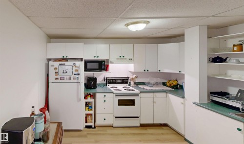 White cabinetry with green hardware, light wood-finish flooring, drop ceiling, white appliances, and open shelving - 10941 81 Avenue Nw, Edmonton, AB 