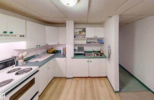 Efficient kitchen layout featuring white cabinetry, a built-in range hood, a double basin sink, light wood-finish flooring, and open shelving - 10941 81 Avenue Nw, Edmonton, AB 