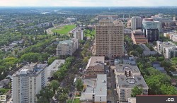 Expansive urban landscape featuring dense residential areas, commercial structures, abundant mature trees, a prominent river, and a large recreational green space - 