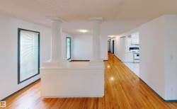 Hardwood-finish flooring, white painted walls, white ceiling, white kitchen cabinetry, and built-in architectural columns - 