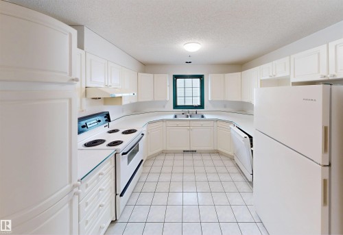 U-shaped kitchen featuring white cabinetry, white tile flooring, white appliances, and a window above the sink - 10941 81 Avenue Nw, Edmonton, AB 
