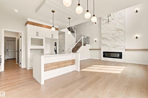 Expansive living area with high ceilings, featuring a floor-to-ceiling fireplace with stone-look surround, a built-in linear fireplace, and wood-finish flooring - 10458 104 Street, Morinville, AB 
