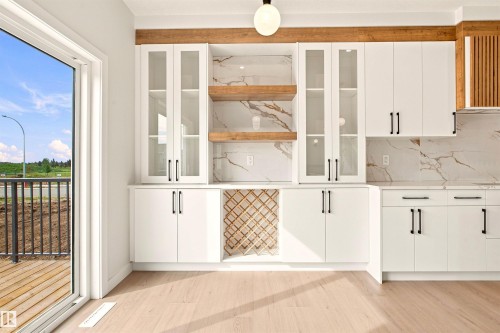 White cabinetry with matte black hardware, integrated wine rack, wood-finish open shelving, and light wood-finish flooring - 10458 104 Street, Morinville, AB 