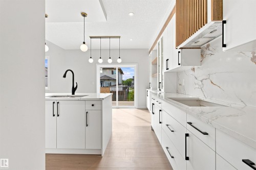 White cabinetry with black hardware, wood-finish flooring, white countertops with veining, and a sliding glass door - 10458 104 Street, Morinville, AB 