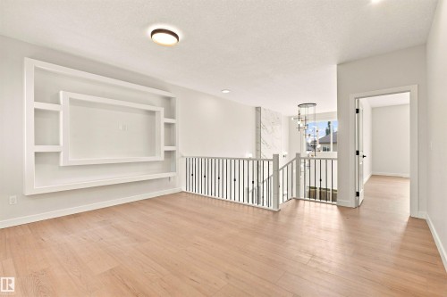 Wood-finish flooring throughout, built-in shelving, white baluster railings, and a contemporary chandelier - 10458 104 Street, Morinville, AB 