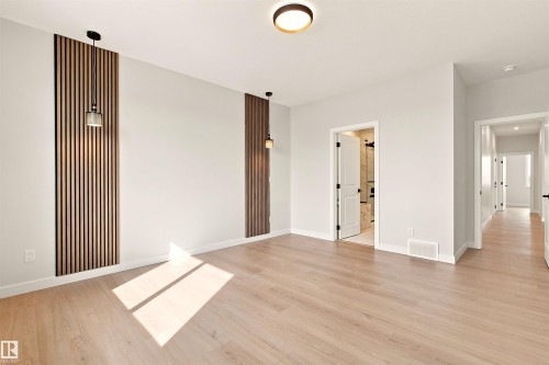 Wood-finish flooring, accent wall panels, contemporary pendant lighting, recessed ceiling lighting, and a white interior door with dark hardware - 10458 104 Street, Morinville, AB 