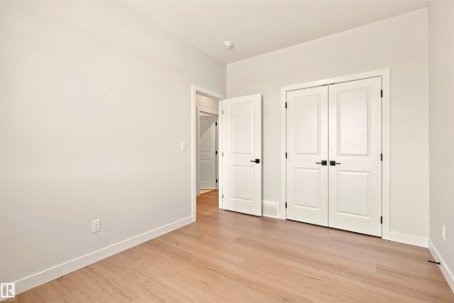 Light wood-finish flooring, white walls, double panel doors with matte black hardware, and a single panel door with matte black hardware - 10458 104 Street, Morinville, AB 