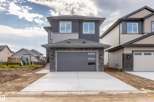 Modern two-story exterior featuring a grey garage door with frosted glass inserts, stone veneer accents, and dark grey siding - 10458 104 Street, Morinville, AB 