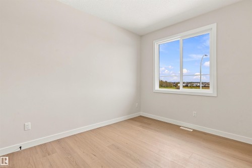 Light-toned walls, wood-finish flooring, and a large window with white trim - 10458 104 Street, Morinville, AB 