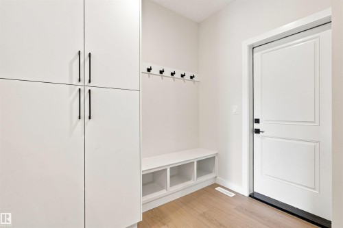 Entry area featuring wood-finish flooring, white built-in storage cabinets with black hardware, a built-in bench with open cubbies, and a row of wall-mounted hooks - 10458 104 Street, Morinville, AB 