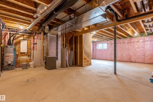 Unfinished basement featuring exposed wood joists, utility systems, a water heater, and a window - 10458 104 Street, Morinville, AB 