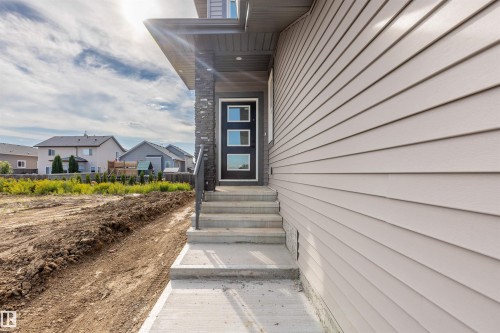 Exterior featuring light-toned horizontal siding, a stone accent column, a contemporary entry door with frosted glass inserts, and a concrete walkway - 10458 104 Street, Morinville, AB 