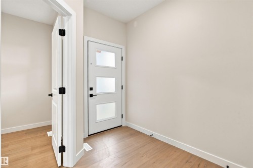 Entryway featuring a contemporary door with three frosted glass panels, matte black hardware, and wood-finish flooring - 10458 104 Street, Morinville, AB 