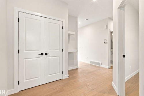 Light wood-finish flooring, white walls, double panel doors with black hardware, and built-in shelving - 10458 104 Street, Morinville, AB 