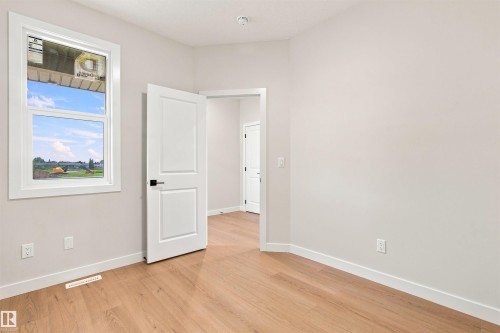 Light wood-finish flooring, white trim, and a white interior door with black hardware - 10458 104 Street, Morinville, AB 