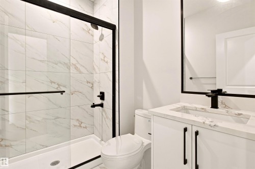 Walk-in shower with clear glass enclosure, white tiled walls with subtle veining, single vanity with white cabinetry, rectangular basin, and matte black fixtures - 10458 104 Street, Morinville, AB 