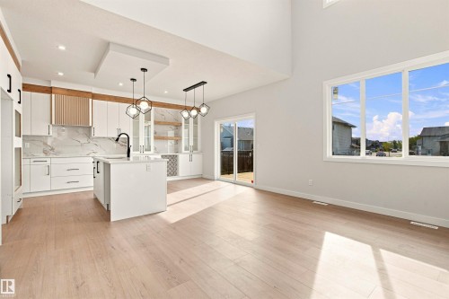 Open concept living space featuring wood-finish flooring, a kitchen island with sink, white cabinetry with integrated appliances, and a sliding glass door leading to the exterior - 10462 104 Street, Morinville, AB 