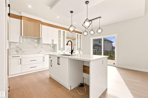 White cabinetry with matte black hardware, integrated kitchen island, coordinating backsplash, wood-finish flooring, and contemporary pendant lighting - 10462 104 Street, Morinville, AB 