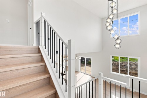 Two-story interior volume with a contemporary chandelier, large windows, wood-finish flooring, and a staircase with white risers and dark balusters - 10462 104 Street, Morinville, AB 