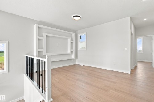 Open-concept room featuring light wood-finish flooring, a built-in entertainment unit with shelving, and large windows - 10462 104 Street, Morinville, AB 