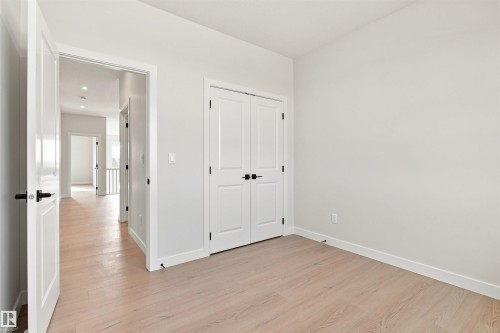 Light wood-finish flooring, white doors with matte black hardware, recessed ceiling lighting, and bright white wall paint - 10462 104 Street, Morinville, AB 