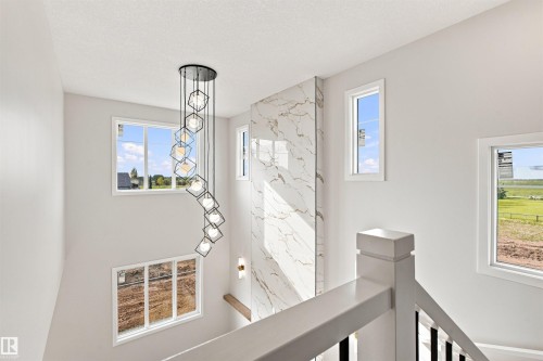Multiple windows, modern spiral chandelier, marble-finish accent wall, and white painted railings - 10462 104 Street, Morinville, AB 