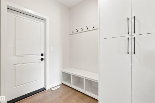 Entryway featuring wood-finish flooring, white paneled door, built-in bench with storage, wall-mounted coat hooks, and integrated white cabinetry - 10462 104 Street, Morinville, AB 
