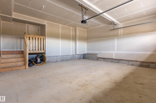 Unfinished garage with concrete flooring, drywall walls, and a wooden staircase featuring a railing - 10462 104 Street, Morinville, AB 