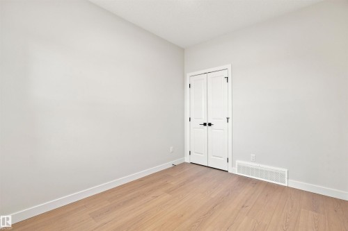 Light wood-finish flooring, white walls, white trim, and white bi-fold doors with black hardware - 10462 104 Street, Morinville, AB 