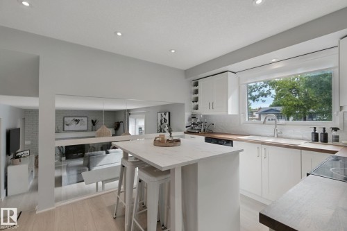 Kitchen featuring white cabinetry, wood-finish countertops, subway tile backsplash, and an integrated kitchen island with seating - 5 Labelle Crescent, St. Albert, AB 