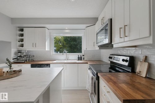 White cabinetry with brushed nickel hardware, light wood-finish countertops, white subway tile backsplash, and a stainless steel over-the-range microwave - 5 Labelle Crescent, St. Albert, AB 