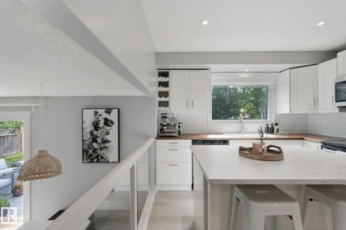White shaker cabinetry with dark hardware, a large kitchen island with counter seating, a stainless steel dishwasher, wood-finish countertops, and recessed lighting - 5 Labelle Crescent, St. Albert, AB 