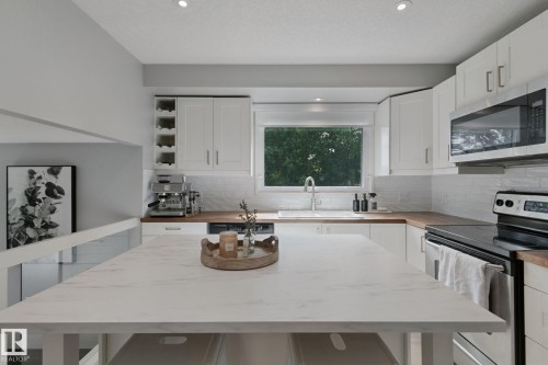 Kitchen featuring white cabinetry, wood-finish countertops, stainless steel appliances, a white subway tile backsplash, and a central island with a light-toned surface - 5 Labelle Crescent, St. Albert, AB 