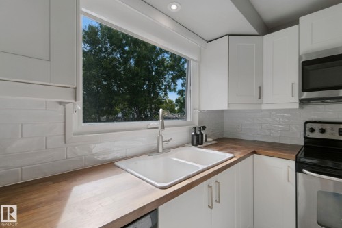 White subway tile backsplash, solid wood countertops, white cabinetry with silver hardware, stainless steel microwave, and a double basin sink - 5 Labelle Crescent, St. Albert, AB 