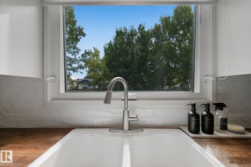 Window over a white apron-front sink with a brushed nickel faucet, set into a wood-finish countertop, complemented by white subway tile backsplash - 5 Labelle Crescent, St. Albert, AB 