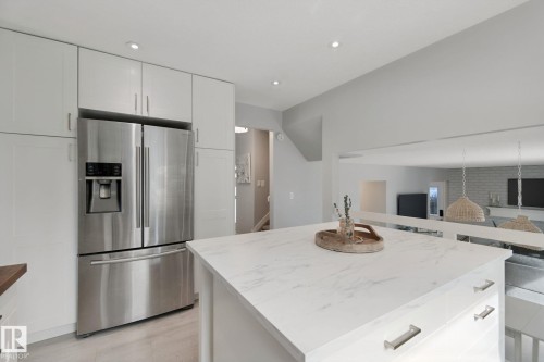 Integrated stainless steel refrigerator, white cabinetry, recessed lighting, and a kitchen island with a light-toned countertop - 5 Labelle Crescent, St. Albert, AB 