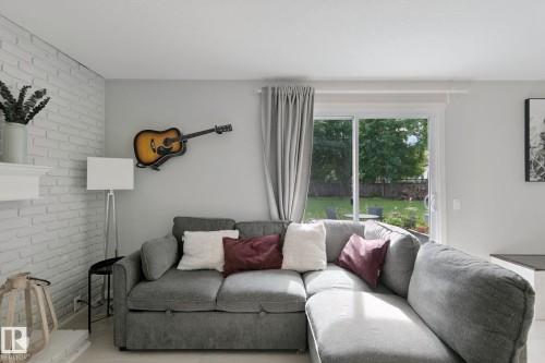 White painted brick accent wall, white mantel, sliding glass door, private backyard with mature trees, and a fenced perimeter - 5 Labelle Crescent, St. Albert, AB 