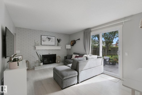 White-washed brick fireplace with a mantel, light wood-finish flooring, and a sliding glass door to the exterior - 5 Labelle Crescent, St. Albert, AB 