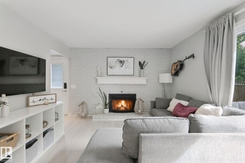 Light-toned wood-finish flooring complements the white brick fireplace with a dark firebox and mantel - 5 Labelle Crescent, St. Albert, AB 