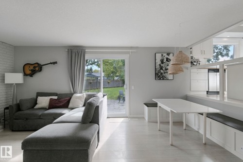 Light wood-finish flooring, sliding glass door, white brick accent wall, white cabinetry, integrated dining area with built-in seating - 5 Labelle Crescent, St. Albert, AB 