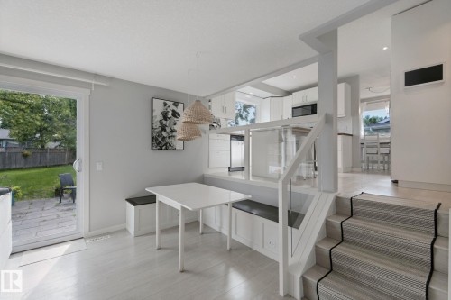 White cabinetry, wood-finish flooring, staircase with a runner, kitchen area with stainless steel appliances, and a sliding glass door to the backyard - 5 Labelle Crescent, St. Albert, AB 