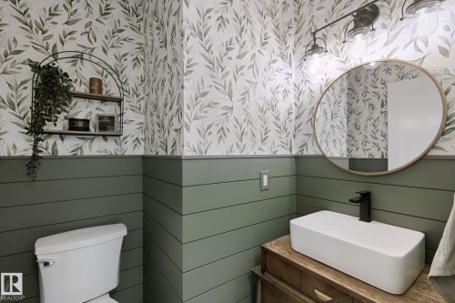 Powder room featuring a rectangular vessel sink, wood-finish vanity, circular mirror, and wall-mounted light fixture - 5 Labelle Crescent, St. Albert, AB 