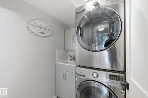 Stacked stainless steel washer and dryer, light gray cabinetry, white sink, and white subway tile backsplash - 5 Labelle Crescent, St. Albert, AB 