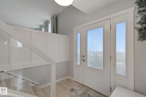 Entryway featuring a paneled door with sidelights, wood-finish flooring, and a contemporary glass panel staircase - 5 Labelle Crescent, St. Albert, AB 