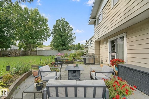 Expansive backyard featuring a stone patio, manicured lawn, perimeter fencing, mature trees, and a sliding glass door - 5 Labelle Crescent, St. Albert, AB 