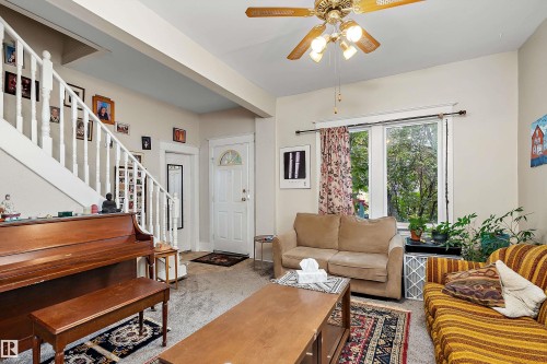 Living area with carpet flooring, a white paneled entry door with an arched transom, a double window, and a ceiling fan - 10816 92 Street Nw, Edmonton, AB 