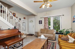 Living area with carpet flooring, a white paneled entry door with an arched transom, a double window, and a ceiling fan - 