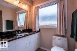 Bathroom featuring a dark granite countertop and white cabinetry, a large mirror, a window with privacy glass, and a toilet - 